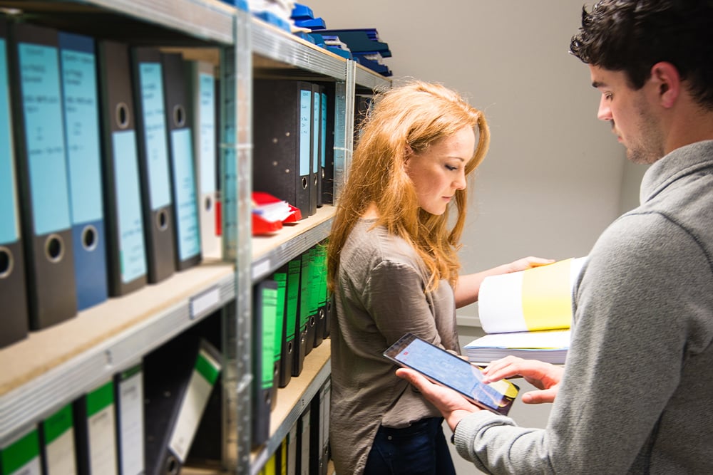 man-mobile-device-woman-perusing-files