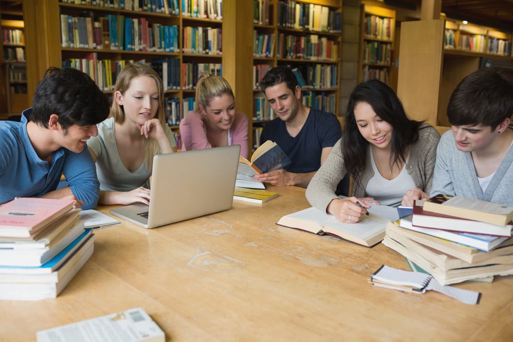 Students sitting at a table in a library while learning and working on a laptop Students sitting at a table in a library while learning and working on a laptop
