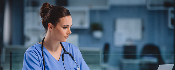female nurse with stethoscope around neck looking at a computer with chart in hand